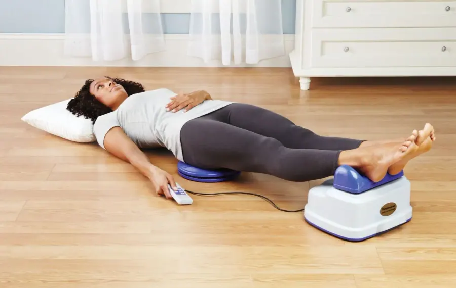 A woman lying on a mat with her ankles resting on a Chi Machine