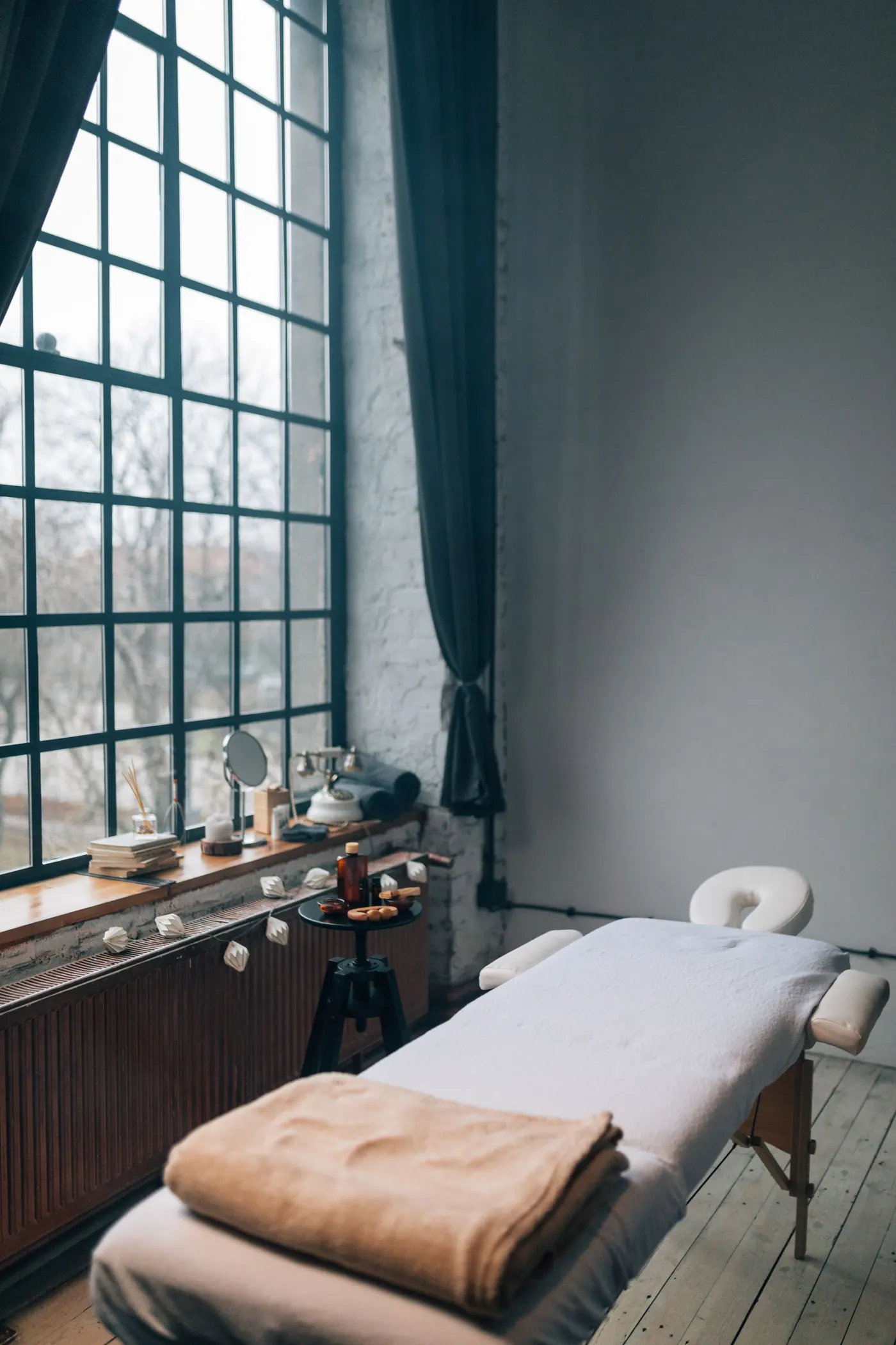 A private treatment room with a massage bed beside a tall window
